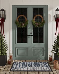 two wreaths on the front door of a house with potted plants and christmas decorations