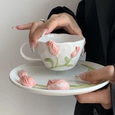 a woman is holding a teacup and saucer with pink flowers on it, while she has her fingers in the cup