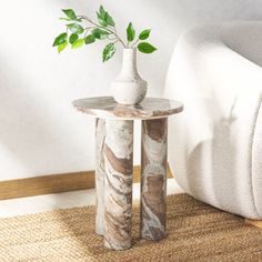 a white vase with a green plant in it sitting on a table next to a couch