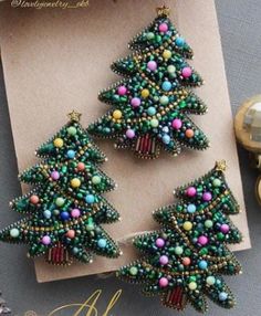 two christmas trees made out of beads on top of a card next to some ornaments