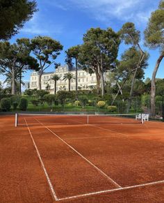 a tennis court in front of a large building with trees on both sides and a white bench at the end