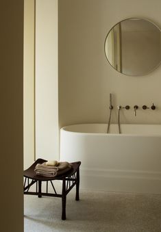 a white bath tub sitting next to a round mirror on the side of a wall