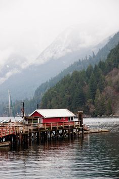 a boat dock with a red building on it's side and mountains in the background