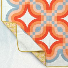 an orange and blue quilt on top of a white blanket