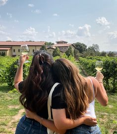 two women hug each other while holding wine glasses in front of their faces and looking at the vineyard