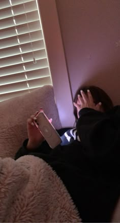 a person laying down on a couch with a book in their hand and looking at the screen