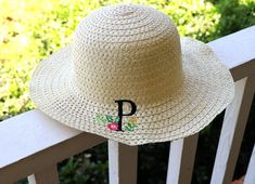 a straw hat with the letter p on it sitting on a wooden deck in front of some bushes