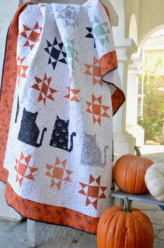 two pumpkins are sitting on the porch next to a quilted cat and star design