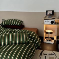 a bed with green and white striped comforter next to a night stand on the floor