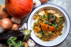 a bowl of food next to an orange and some onions on a table with other vegetables