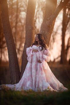 a woman in a pink dress standing next to some trees