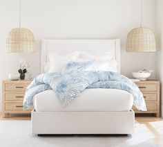 a white bed with blue and white comforter in a bedroom next to two lamps