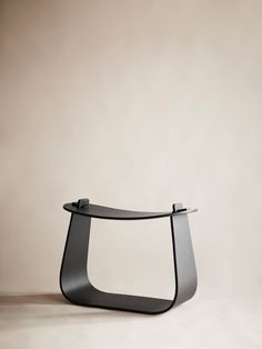 a black table with a curved glass shelf on it's side, in front of a beige wall