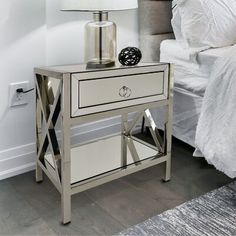 a nightstand with a lamp on top of it next to a bed and a white comforter