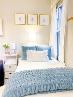 a bed with blue blankets and pillows in a bedroom next to a window on the wall