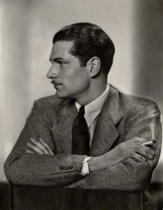 a man in a suit and tie leaning on a table with his arms crossed looking off to the side