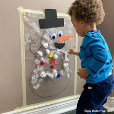 a young boy painting a snowman on a bulletin board with magnets attached to it