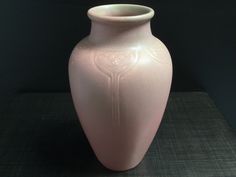 a pink vase sitting on top of a table next to a black wall and floor