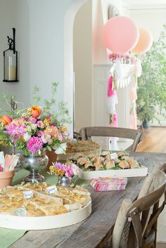 a table filled with food and flowers on top of a wooden table next to a window