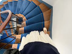 a person is walking up the stairs in a building with blue carpet and wooden handrails