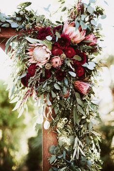 a wedding arch decorated with red flowers and greenery for the bride's bouquet