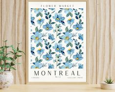 a blue flower market poster hanging on a wall next to a plant and potted plant