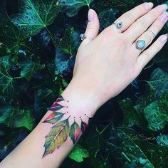 a woman's hand with a leaf tattoo on her left wrist and two rings