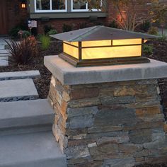 a lit up lantern on top of a stone pillar in front of a brick house