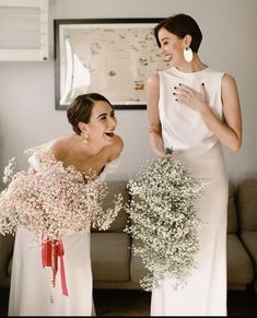 two women standing next to each other in front of a couch with flowers on it