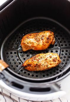 two pieces of chicken cooking in an air fryer with the lid open and on