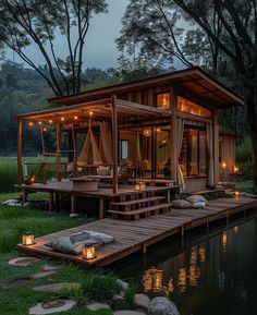 a small wooden cabin with lights on the porch and deck next to a body of water