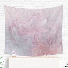 a pink and grey wall hanging over a white dresser next to a potted plant