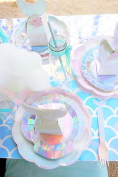 the table is set with plates, cups and utensils for an understaffed mermaid party