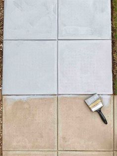 a tile floor with a paintbrush on it and grass growing in the corner next to it