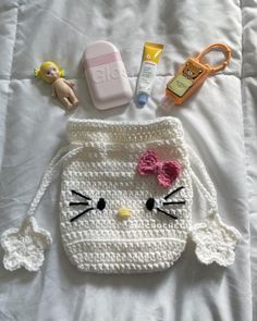 a crocheted hello kitty purse is laying on a bed with toys and other items