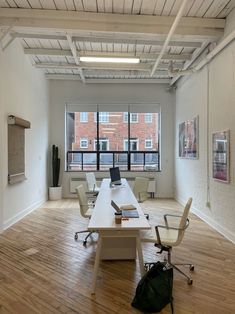 an empty office with wooden floors and white desks in front of large windows on the wall