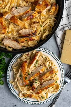 two plates of pasta with chicken and parmesan cheese on the side, next to a cast iron skillet