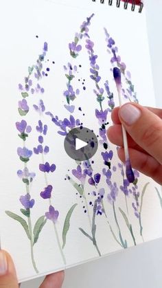 someone is holding a pencil and drawing lavender flowers on a piece of paper with watercolor