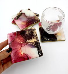 a hand is holding a glass and two square coasters on a table with a drink in the background