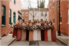 a group of women standing next to each other in front of brick buildings holding bouquets