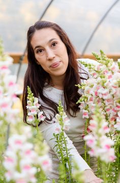 a woman standing in a greenhouse surrounded by pink and white flowers