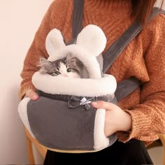 a woman holding a cat in a bag with ears on it's head and wearing a bunny hat