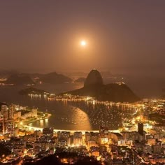 the full moon shines brightly in the sky over a city at night with mountains and water