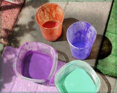 three buckets filled with colored paint sitting on top of a cement floor next to a sidewalk