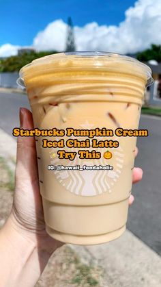 someone holding up a cup of starbucks pumpkin cream iced coffee in front of a street