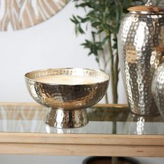 a silver bowl sitting on top of a table next to two vases and a potted plant