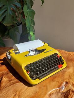 a yellow typewriter sitting on top of a wooden table next to a potted plant