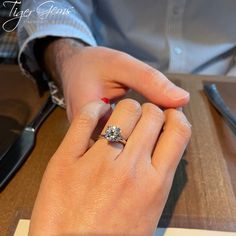 a woman's hand with a diamond ring on top of her finger, sitting at a table