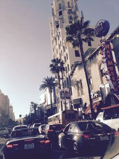 cars are parked on the side of the road in front of tall buildings and palm trees