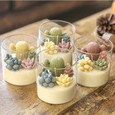 four small glass cups filled with different types of desert plants on top of a wooden table